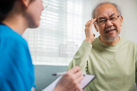 Téléchargez les photos : Asiatique homme âgé patient ont mal à la tête et infirmière parler, vérifier et enregistrer les symptômes actuels sur presse-papiers dans le salon, les soins à domicile et les services médicaux - en image libre de droit