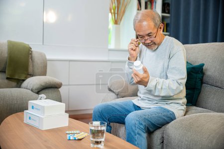 Téléchargez les photos : Asiatique inquiet homme âgé avec des pilules de médecine à prendre sur la table dans le salon, vieil homme acheter à base de plantes auto remède pilule Rx en ligne de la pharmacie, isolement à domicile, service d'aide aux soins de santé - en image libre de droit
