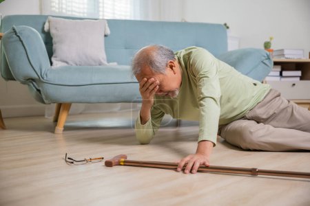 Téléchargez les photos : Malade vieillard tombant couché sur le sol parce que trébuché à la maison seul avec bâton de marche en bois dans le salon, vieillard homme grand-père ayant un accident tout en marchant avec marcheur de canne - en image libre de droit