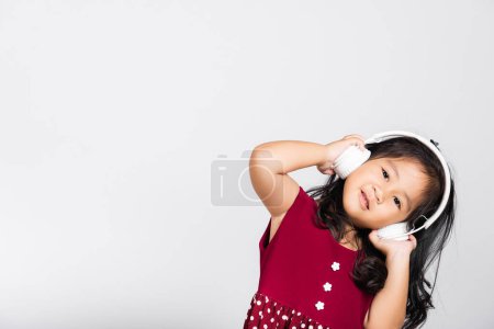 Foto de Niña linda niño 3-4 años escuchar música en auriculares inalámbricos en estudio tiro aislado sobre fondo blanco, niños asiáticos felices sonriendo escuchar audio, estilo de vida de entretenimiento - Imagen libre de derechos
