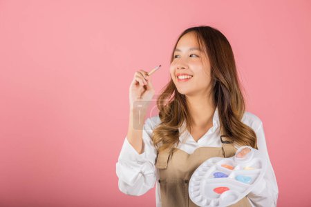 Photo for Asian beautiful young woman artist holding brush and paint palette, Happy female painting using paintbrush and palette with colors, studio shot isolated on pink background, Paintings and art equipment - Royalty Free Image