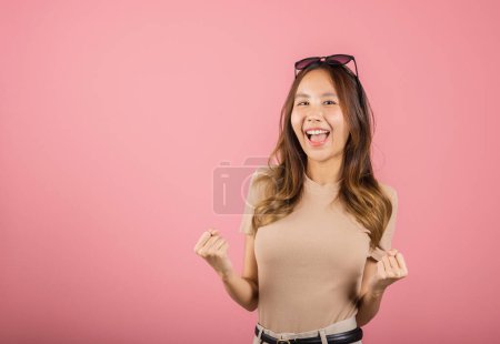 Photo for Happy Asian portrait beautiful cute young woman wear glasses makes raised hand up celebrating her winning success gesture, studio shot isolated pink background, Female excited say yes with copy space - Royalty Free Image