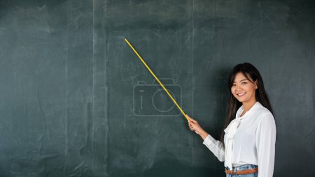 Photo for Back to school concept. Happy beautiful young woman standing hold pointer to back board, Asian female teacher smiling with wooden stick pointing to blackboard at school in classroom, Education - Royalty Free Image