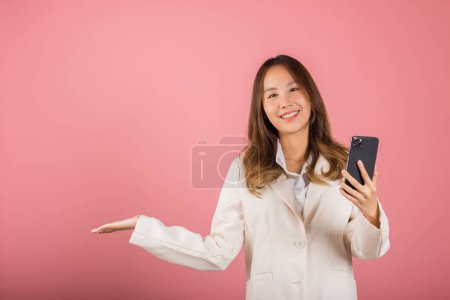 Téléchargez les photos : Happy Asian portrait beautiful cute young woman excited holding mobile phone blank screen presenting product with palm of hand at empty, studio shot isolated on pink background, female look camera - en image libre de droit