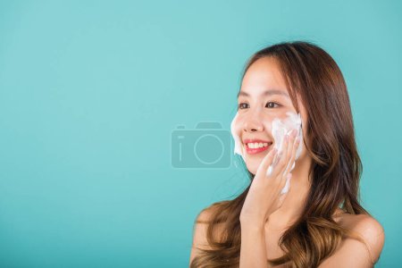 Photo for Portrait beautiful female smile applies foaming cleanser healthy skin, Asian women face wash exfoliating scrub soap with skincare cleansing, Studio isolated on blue background, skincare daily routine - Royalty Free Image