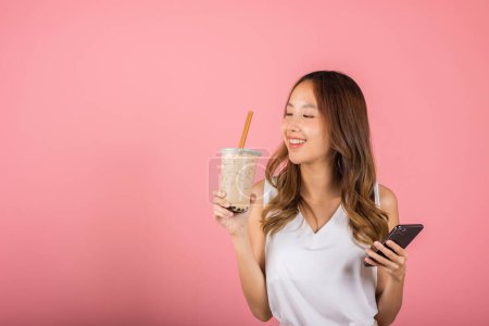 Photo for Asian beautiful young woman holding drinking brown sugar flavored tapioca pearl bubble milk tea and mobile phone, Portrait female, studio shot isolated on pink background, milk beverage concept - Royalty Free Image