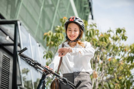 Téléchargez les photos : Portrait femme souriante vérifier montre, Asiatique jeune femme d'affaires debout avec vélo vérifier horloge heure sur la rue de la ville urbaine le matin aller au travail au bureau, Transport de banlieue d'affaires - en image libre de droit