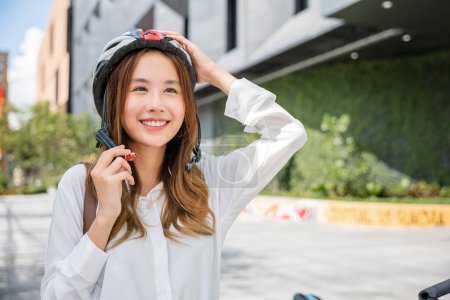 Photo for Asian young businesswoman putting biking helmet prepared cyclists go to work, Close up beautiful woman wearing helmet exercise outdoors, Transport Save Energy concept - Royalty Free Image