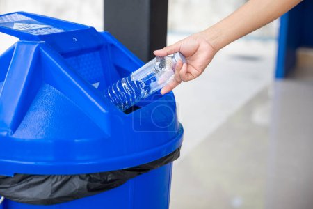 Téléchargez les photos : Close up female throwing empty bottle to trash, woman hand throwing empty plastic water bottle into blue recycling bin, Recycle rubbish, separate for save the world and environment care - en image libre de droit