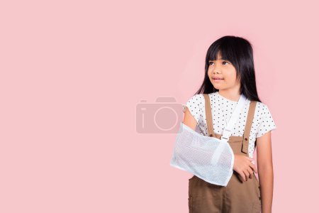 Foto de Arm broken. Asian little kid 10 years old hand bone broken from accident with arm splint at studio shot isolated on pink background, Happy child girl accident insurance and extreme sports speed - Imagen libre de derechos