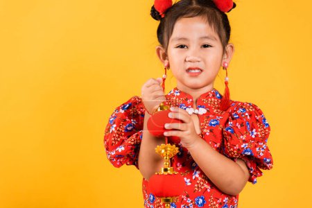 Téléchargez les photos : Nouvel An chinois. Happy Asian Chinese little girl smile wearing red cheongsam qipao holding silk lanterns on hand, Portrait enfants en robe traditionnelle, studio court isolé sur fond jaune - en image libre de droit