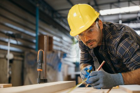 Photo for Carpenter man wear gloves during working using tape measure and pencil to make marks piece of wood board for cut on table saw at workshop or woodshop industry, woodwork, Happy Carpenters Day - Royalty Free Image