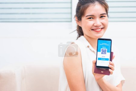 Téléchargez les photos : Asian young woman smile have adhesive plaster on arm her vaccinated and showing app smartphone mobile digital screen vaccinated coronavirus COVID-19 certificate after getting vaccine prevent - en image libre de droit