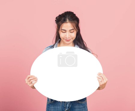 Téléchargez les photos : Heureuse asiatique belle jeune femme souriante vêtements excités denims tenant vide bulle de parole signe, Portrait femelle posant apparaître pour votre idée en regardant la bulle, studio tourné isolé sur fond rose - en image libre de droit