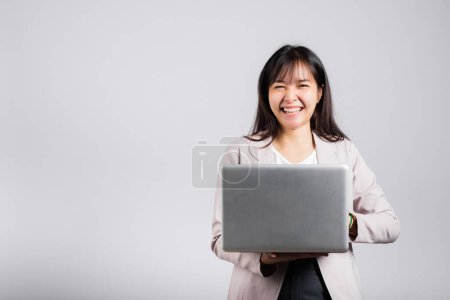 Téléchargez les photos : Femme souriante confiante souriante tenant à l'aide d'un ordinateur portable et dactylographier clavier pour l'envoi en ligne e-mail ou chat, Portrait excité heureux asiatique jeune studio féminin tourné isolé sur fond blanc - en image libre de droit