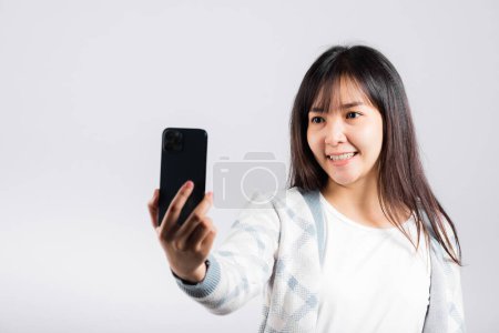 Téléchargez les photos : Femme excitée tenant smartphone pour prendre des photos selfie caméra avant studio tourné fond blanc isolé, heureux jeune femme souriant prendre des photos par téléphone mobile sur téléphone mobile - en image libre de droit