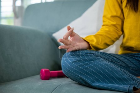 Photo for Young woman practise yoga and meditation in lotus position, mindfulness lifestyle, Asian female sits on sofa at home and chilling do yoga exercise with couch lotus pose eyes closed, healthy care - Royalty Free Image
