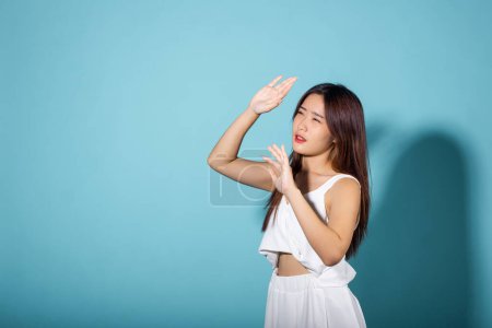 Photo for Female raising arm and hand in protection and block sunshine in studio shot isolated on blue background, Asian young woman smile hand up cover face protect sun light and UV, sunscreen cream advertise - Royalty Free Image