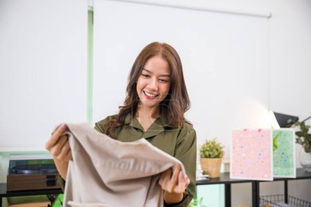Téléchargez les photos : Happy Asian young customer woman opening shopping bag package after ordered new fashion clothes at home, shopping online from home, Excited smile female shopper holding shirt - en image libre de droit