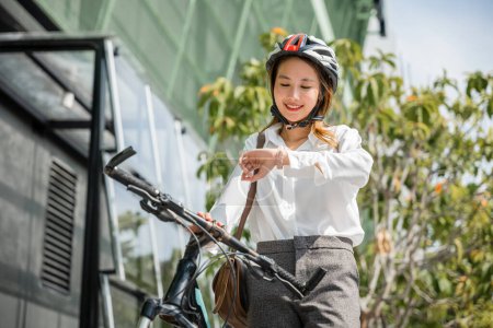 Téléchargez les photos : Portrait femme souriante check watch, Asiatique jeune femme d'affaires debout avec vélo vérifier l'heure sur les bâtiments modernes rue de la ville le matin avant d'aller au travail au bureau, Commutateur d'affaires, mode de vie - en image libre de droit