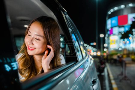 Téléchargez les photos : Asian businesswoman working late commuting from office in Taxi backseat with mobile phone in city at night after late work, Happy beautiful woman texting smartphone sitting car back seat in urban - en image libre de droit