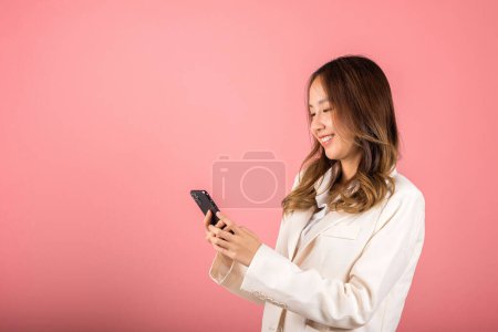 Foto de Female surprised and sms chatting internet online on smartphone studio shot isolated on pink background, Happy Asian portrait beautiful cute young woman teen smiling excited hold smart mobile phone - Imagen libre de derechos