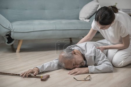 Téléchargez les photos : Asie jeune femme haltant son père après être tombé sur le sol, vieil homme âgé avec bâton de marche tomber sur le sol et camp de fille pour aider à la maison dans le salon, les soins de santé familiale - en image libre de droit