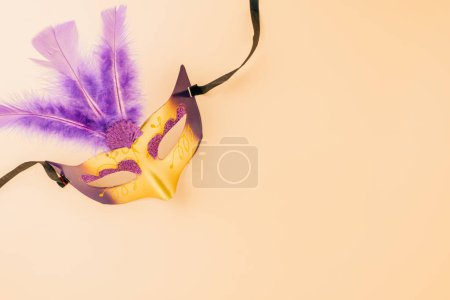 Fröhliche Purimkarnevalsdekoration. Draufsicht venezianische Ballmaske mit lila Federn auf pastellfarbenem Hintergrund, jüdisches Purim und Mardi Gras auf Hebräisch, Feiertagshintergrundbanner Design, Maskenparty