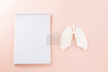 Photo for World Tuberculosis Day. Overhead lungs paper symbol, medical stethoscope and notebook paper on pastel pink background, lung cancer awareness, copy space concept of world TB day - Royalty Free Image
