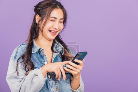 Photo for Portrait of Asian beautiful young woman confident wear denim jeans shirt hold smartphone typing smartphone, Happy lifestyle female write message look phone, studio shot isolated on purple background - Royalty Free Image