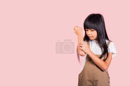 Foto de Niño asiático 10 años de edad rascarse el brazo picazón de una picadura de mosquito en el estudio tiro aislado sobre fondo rosa, Retrato de niña feliz dermatitis y sarna, Síntomas de alergia, día de la malaria - Imagen libre de derechos