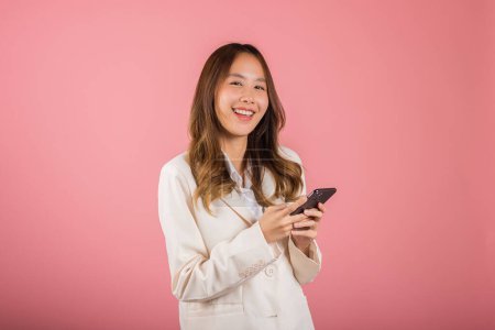 Téléchargez les photos : Female surprised and sms chatting internet online on smartphone studio shot isolated on pink background, Happy Asian portrait beautiful cute young woman teen smiling excited hold smart mobile phone - en image libre de droit