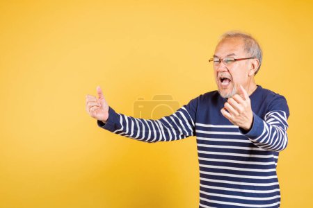 Foto de Feliz asiático anciano hombre con gafas emocionado decir sí gesto como ganador estudio disparo aislado en amarillo fondo, retrato sonriente anciano estilo de vida que brazos levantó para celebrar su éxito - Imagen libre de derechos
