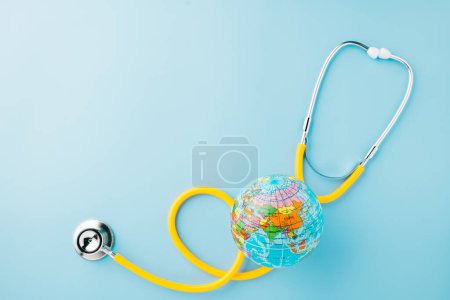 Photo for World Health Day. Top view yellow doctor stethoscope wrapped around world globe isolated on pastel blue background with copy space for text, Save world day, Health care and medical concept - Royalty Free Image