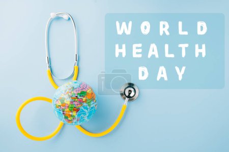 Téléchargez les photos : World Health Day Concept. Top view yellow doctor stethoscope and world globe isolated on pastel blue background with copy space, Save world day, Environment Green Earth, Health care and medical - en image libre de droit