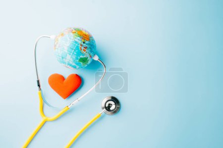 Photo for World Health Day. Yellow doctor stethoscope and world globe with Red heart shape isolated on blue background with copy space, Save world day, Green Earth Environment, Healthcare and medical concept - Royalty Free Image