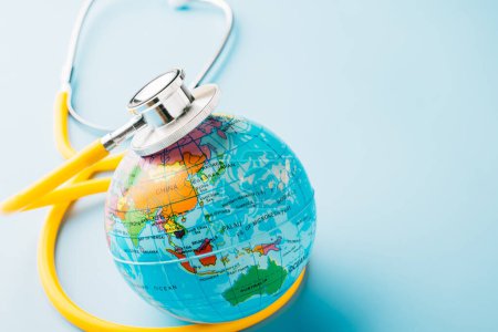 Téléchargez les photos : World Health Day. Top view yellow doctor stethoscope wrapped around world globe isolated on pastel blue background with copy space for text, Save world day, Health care and medical concept - en image libre de droit