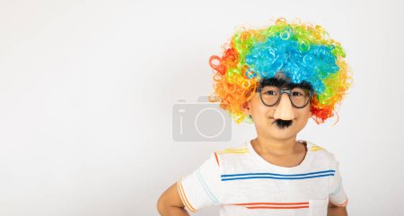 Foto de Día de los Inocentes. Retrato de niño divertido payaso usa una peluca rizada colorido a grandes nos y gafas y tiene un bigote aislado sobre fondo blanco con espacio para copiar, Feliz decoración festiva infantil - Imagen libre de derechos