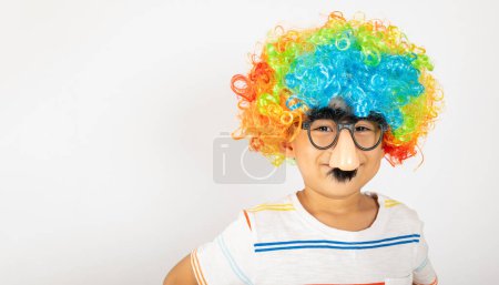 Photo for April Fools Day. Portrait of Funny kid boy clown wears a curly wig colorful a big nos and glasses and has a mustache isolated on white background with copy space, Happy child festive decor - Royalty Free Image