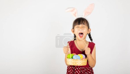 Photo for Happy Easter Day. Smile Asian little girl wearing easter bunny ears holding basket of full colorful eggs smiles broadly isolated on white background with copy space, Happy child in holiday - Royalty Free Image