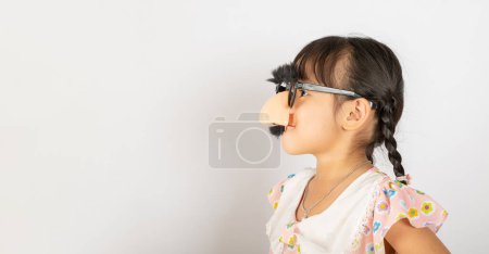 Foto de Día de los Inocentes. Retrato de niño divertido payaso niña lleva un nos grande y gafas y tiene un bigote aislado sobre fondo blanco con espacio de copia, Feliz sonrisa decoración festiva infantil - Imagen libre de derechos