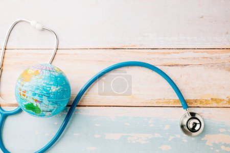 Téléchargez les photos : World Health Day. Top view doctor stethoscope wrapped around world globe isolated on wooden background with copy space for text, Save world day, Health care and medical concept - en image libre de droit