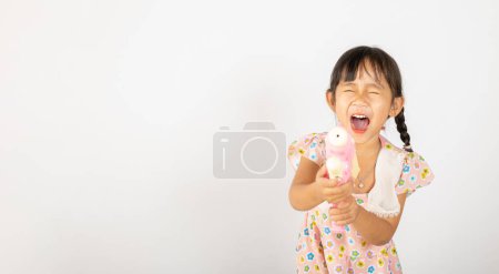 Téléchargez les photos : Happy Songkran Day, Asiatique petite fille tenant pistolet à eau en plastique, enfant thaïlandais drôle tenir jouet pistolet à eau et sourire, isolé sur fond blanc, Thaïlande Songkran festival concept de culture nationale - en image libre de droit