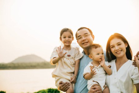 Photo for Portrait of happy family enjoying a beautiful spring day in park, with their cute baby and lovely nature surrounding them outdoor. young couple holding their adorable baby and enjoying stunning sunset - Royalty Free Image