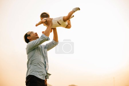 Téléchargez les photos : Par un jour de printemps dans la nature, un père aimant tient sa petite fille haut dans le parc. La petite fille lève les bras dans une liberté ludique, profitant d'un moment d'amour et de bonheur avec son père - en image libre de droit