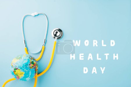 Día Mundial de la Salud. Top view estetoscopio médico amarillo envuelto en todo el mundo aislado sobre fondo azul pastel con espacio de copia para texto, salud global, cuidado de la salud y concepto médico