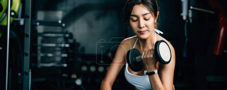 Photo for A fitness enthusiast sitting on a gym bench and lifting dumbbells to improve her strength and power for effective weightlifting training, fitness GYM dark background - Royalty Free Image