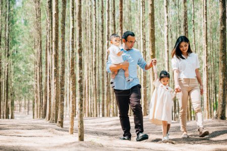 Téléchargez les photos : Les parents et leurs enfants s'amusent pendant les vacances d'été, marchent dans un parc avec vue sur les beaux arbres, Bonne journée familiale - en image libre de droit