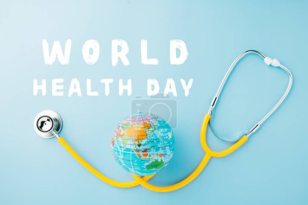 Foto de World Health Day. Yellow doctor stethoscope and world globe isolated on pastel blue background with copy space for text, Save world day, Green Earth Environment, Healthcare and medical concept - Imagen libre de derechos