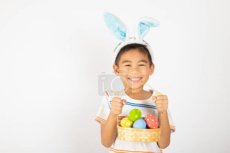 Photo for Happy Easter Day. Smile Asian little boy wearing easter bunny ears holding basket of full colorful eggs smiles broadly isolated on white background with copy space, Happy child in holiday - Royalty Free Image